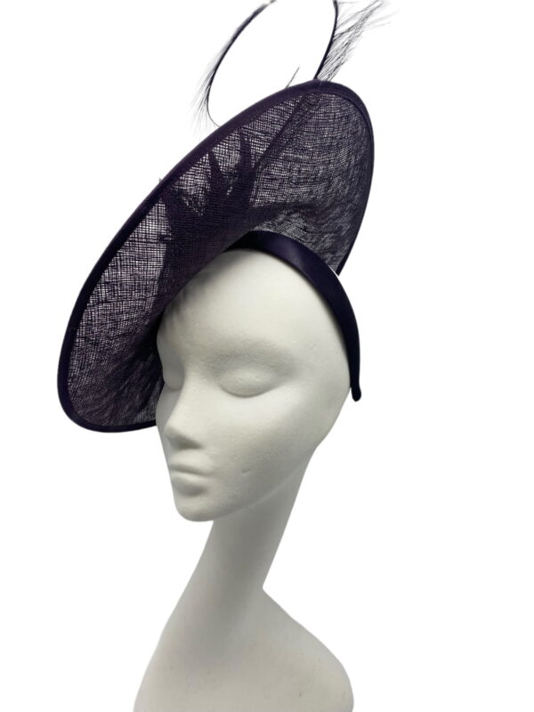 Purple saucer style headpiece with pewter embellishment to the side finished with a spray of colour matching feathers.